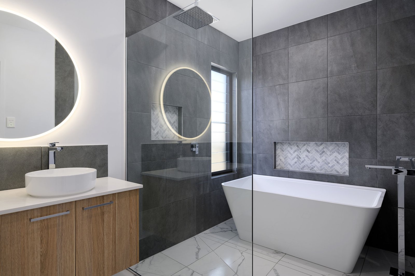 Ultra-modern bathroom showcases a square trapezoid bathtub, complemented by slate grey tiles, a wooden cabinet, and a back-lit mirror